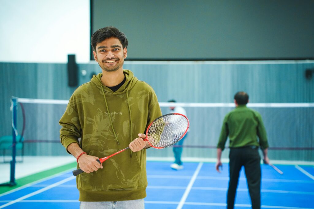 pexels photo 36285087 36285087 Portrait of a young man holding a badminton racket indoors, ready to play.